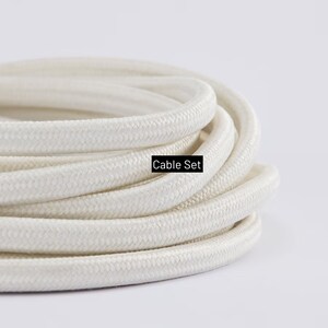 May include: Coiled white cable set with a woven texture. The text "Cable Set" is displayed in a black rectangle. The cable is a neutral color, suitable for various applications.