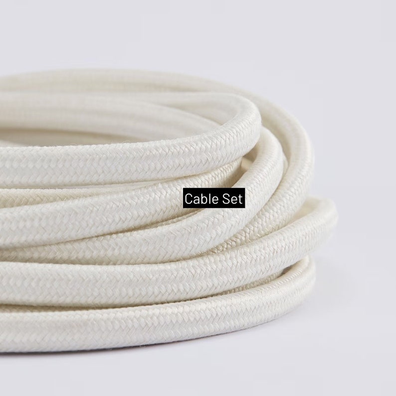 May include: Coiled white cable set with a woven texture. The text "Cable Set" is displayed in a black rectangle. The cable is a neutral color, suitable for various applications.