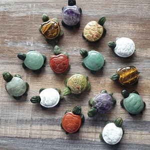 May include: A collection of 14 small turtle figurines carved from various types of stone. The turtles are in different colours, including green, red, white, purple, and brown.