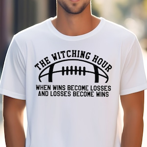Op de afbeelding: Wit T-shirt met een zwarte afbeelding van een voetbal en de tekst "The Witching Hour When Wins Become Losses And Losses Become Wins".