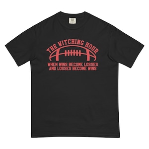 Op de afbeelding: Zwart T-shirt met een rode afbeelding van een voetbal en de tekst "The Witching Hour When Wins Become Losses And Losses Become Wins".