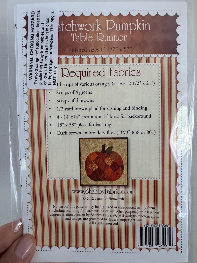 May include: A package for a "Patchwork Pumpkin Table Runner" with a finished size of 12 1/2" x 53". The package includes a list of required fabrics, including orange, green, and brown fabrics. A small image of a patchwork pumpkin is featured.