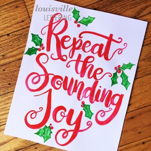 May include: Red and green watercolor calligraphy on white paper with the text "Repeat the Sounding Joy". The text is surrounded by green holly leaves and red berries.