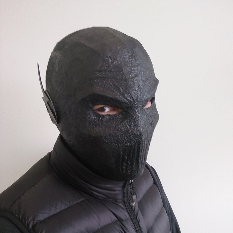 May include: A black mask with a textured surface and a raised ear piece. The mask covers the entire head and has eye holes.