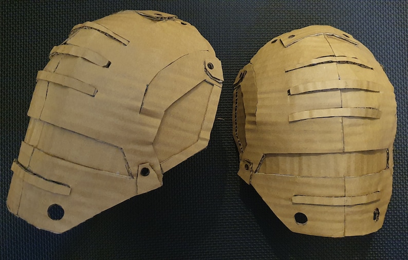 May include: Two brown cardboard pieces, possibly for a costume, with cutouts and holes. The pieces are shaped like shoulder pads.