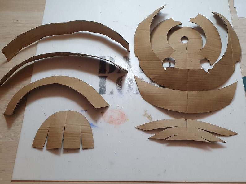 May include: A set of cardboard pieces for crafting a model. The pieces are brown and have various shapes, including circles, arches, and curved lines.