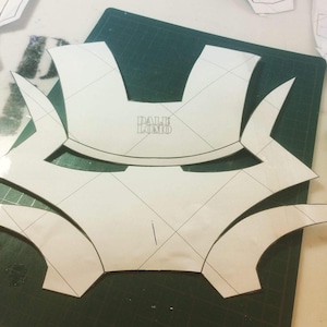 May include: A white paper pattern for a mask with a grid pattern and the text "DALE LOMO" in the center.