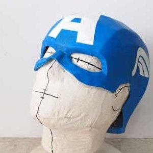 K&ouml;nnte beinhalten: Eine blaue und wei&szlig;e Captain America Maske mit einem wei&szlig;en Stern auf der Vorderseite. Die Maske besteht aus einem weichen, flexiblen Material und ist so konzipiert, dass sie bequem auf dem Kopf sitzt.