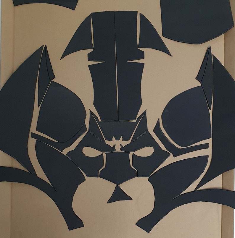 May include: Black paper craft template for a mask with a geometric design. The mask has a pointed top and a wide, flat bottom. The mask is made up of several pieces that are cut out and assembled.