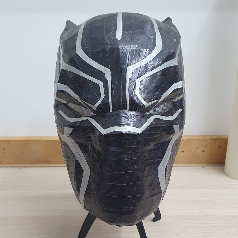 May include: Black and silver papier-m&acirc;ch&eacute; mask of a superhero with a geometric design. The mask is made of paper and tape and has a three-dimensional shape.