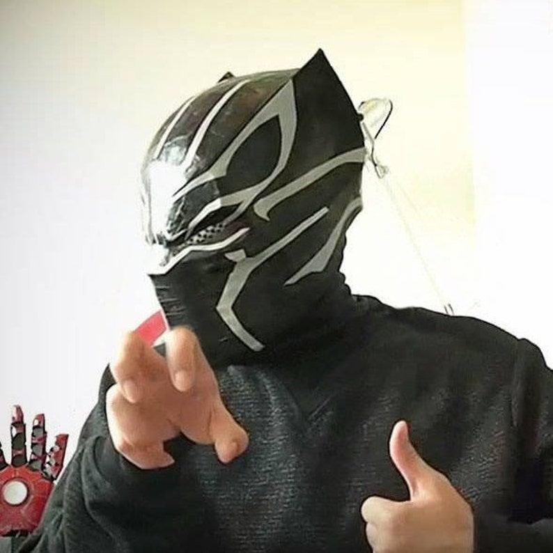May include: A person wearing a black and silver mask with a black turtleneck shirt. The mask has a design that resembles a panther.