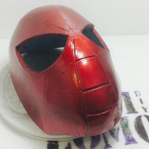 May include: Red and black plastic mask with a textured surface. The mask has a spider-web design and eye holes.