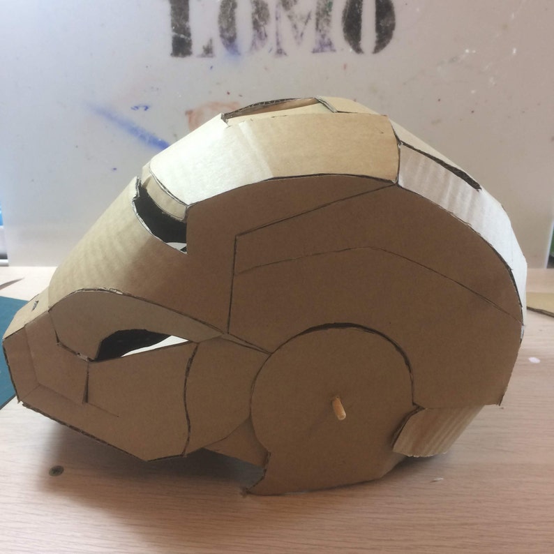 May include: A cardboard model of a helmet, possibly inspired by the Iron Man character, with a brown color and visible details of the design.