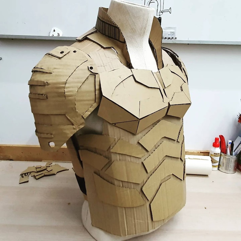 May include: A cardboard chest piece and shoulder pads for a costume. The armor is made of cardboard and is designed to look like a futuristic or fantasy warrior.