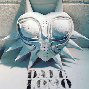 May include: A white, heart-shaped mask with a spiky, starburst design. The mask has two large, round eyes and a detailed, intricate design.