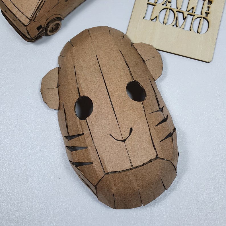 Peut inclure: Un masque en carton brun avec deux yeux noirs, un petit sourire et des marques ray&eacute;es sur les c&ocirc;t&eacute;s. Le masque est fait de carton et a une surface textur&eacute;e.