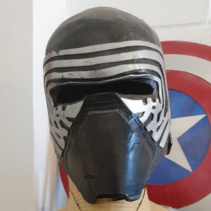 May include: A black and silver Kylo Ren helmet with a textured surface and a raised design. The helmet has a black visor and a silver trim.