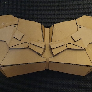 May include: A cardboard cutout of a symmetrical design with two wings on each side. The cutout is brown and has a textured surface.
