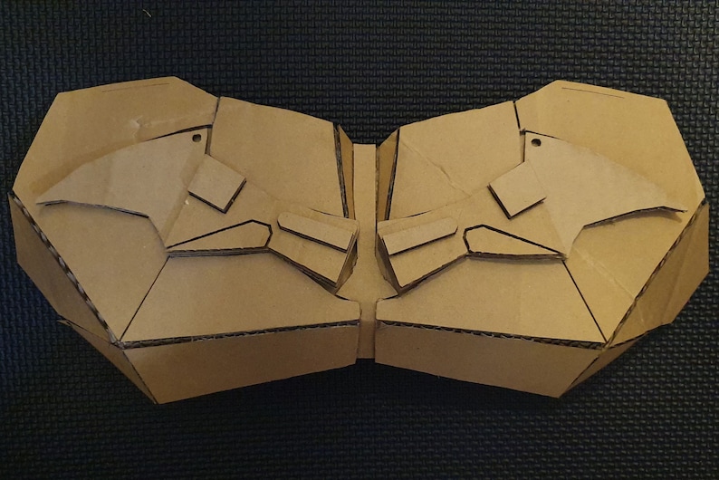 May include: A cardboard cutout of a symmetrical design with two wings on each side. The cutout is brown and has a textured surface.