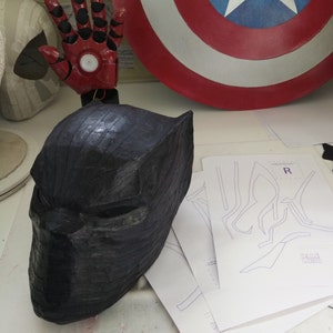 May include: A black, textured, paper mache Black Panther mask. The mask has a detailed design and is a popular character from Marvel Comics.