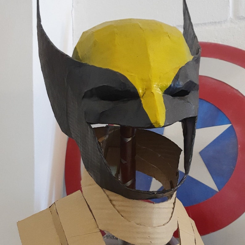 May include: A black and yellow cardboard mask of Wolverine, a superhero from the X-Men comics. The mask is on a cardboard stand and has a cutout for the eyes and mouth.