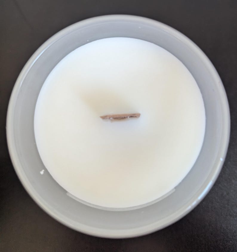 May include: A white candle in a clear glass jar with a wooden wick. The candle is unlit and the wick is visible.