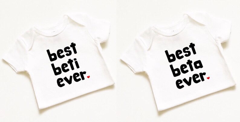 May include: Two white baby onesies with black text. One onesie says "best beti ever" with a small red heart. The other onesie says "best beta ever" with a small red heart.