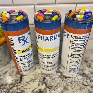 May include: Three colorful pill-shaped tumblers with a prescription label design. The labels read "Rx Pharmacy", "April A", and "Take One Tablet Twice Daily".
