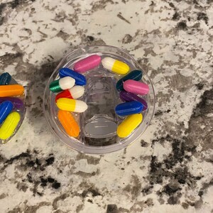May include: A clear plastic container filled with colorful capsule-shaped beads. The beads are in various colors, including red, blue, green, yellow, orange, and purple.