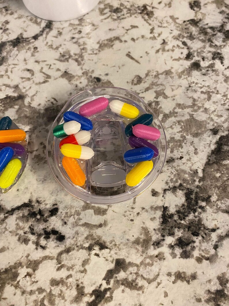 May include: A clear plastic container filled with colorful capsule-shaped beads. The beads are in various colors, including red, blue, green, yellow, orange, and purple.