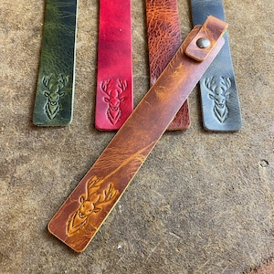 K&ouml;nnte beinhalten: Vier Leder-Lesezeichen mit einem Hirsch-Design. Die Lesezeichen sind in Gr&uuml;n, Rot, Braun und Hellbraun. Das hellbraune Lesezeichen liegt auf den anderen.
