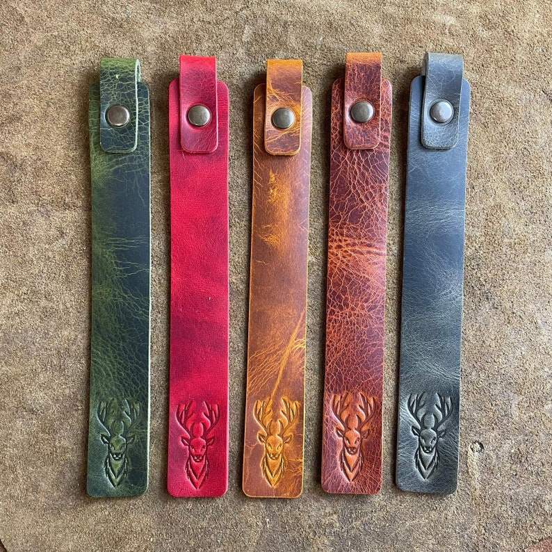 K&ouml;nnte beinhalten: F&uuml;nf Leder-Lesezeichen mit einem Hirschkopf-Design. Die Lesezeichen sind in Gr&uuml;n, Rot, Braun, Braun und Blau.