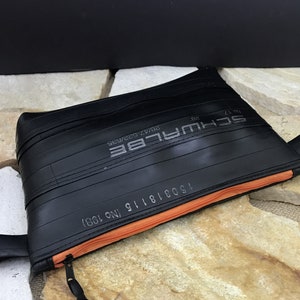 May include: A black zippered pouch made from recycled bicycle inner tubes. The pouch has an orange zipper and the text "SCHWALBE 28x1.75 30psi 622mm 15001816 NO.1981" printed on the front.