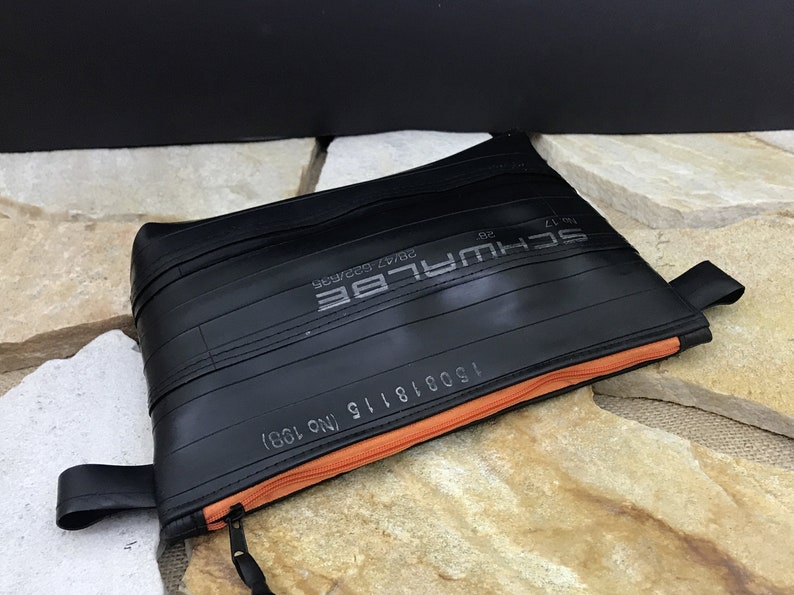 May include: A black zippered pouch made from recycled bicycle inner tubes. The pouch has an orange zipper and the text "SCHWALBE 28x1.75 30psi 622mm 15001816 NO.1981" printed on the front.