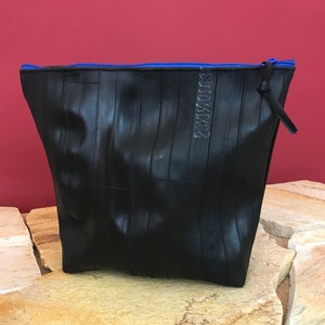 May include: Black zippered pouch made from recycled tire inner tubes. The pouch has a blue zipper and the text "RECYCLED" is visible on the front.