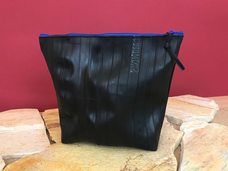 May include: Black zippered pouch made from recycled tire inner tubes. The pouch has a blue zipper and the text "RECYCLED" is visible on the front.