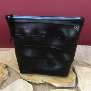 May include: Black zippered pouch made from recycled tire inner tubes. The zipper is light blue.