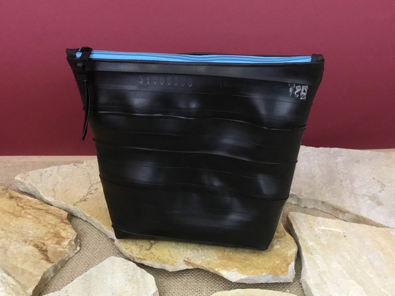 May include: Black zippered pouch made from recycled tire inner tubes. The zipper is light blue.