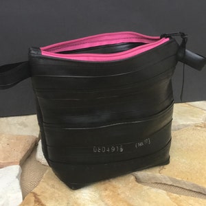 May include: Black zippered pouch made from recycled tire inner tubes with a pink zipper and a black strap. The pouch has a white label with the text "0604918 (No. 17)"