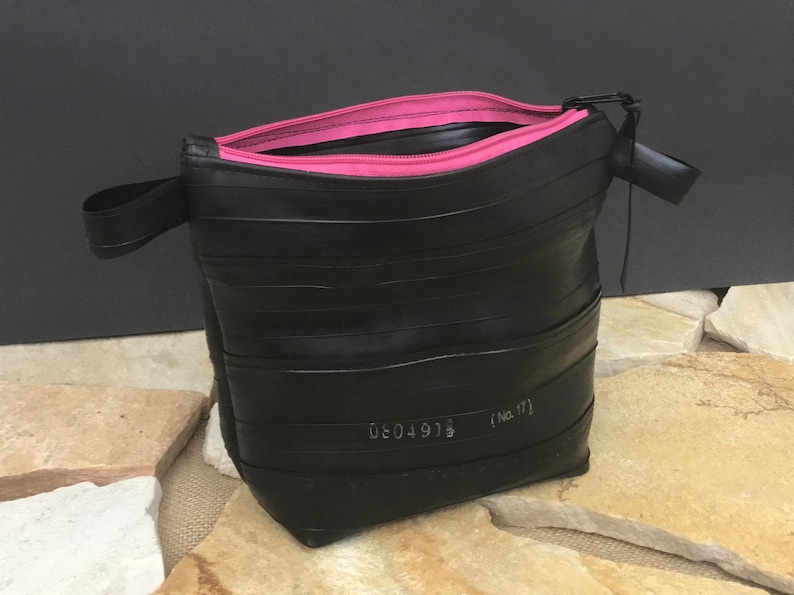 May include: Black zippered pouch made from recycled tire inner tubes with a pink zipper and a black strap. The pouch has a white label with the text "0604918 (No. 17)"