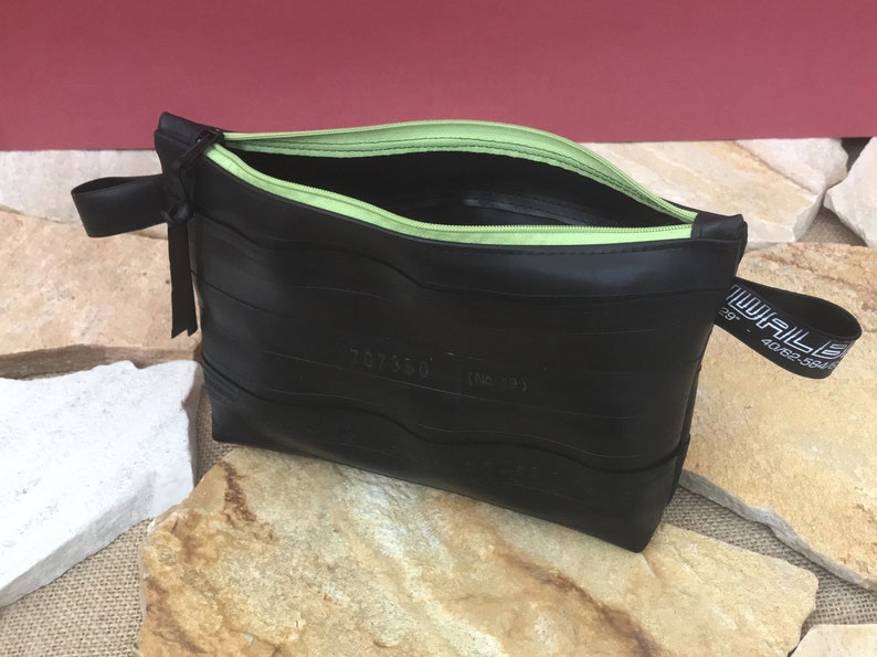 May include: Black zippered pouch made from recycled tire inner tubes with a green zipper and a black strap with the text "WALL 40.62" printed on it.
