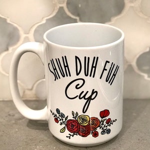 May include: White ceramic mug with a black floral design and the text "Shuh duh fuh cup".