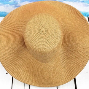 May include: A wide-brimmed straw sun hat in a light brown color. The hat has a woven texture and a slightly rounded crown.