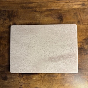 Könnte beinhalten: Ein rechteckiges, hellgraues Schneidebrett aus Marmor mit einem gesprenkelten Muster. Das Brett hat abgerundete Ecken und eine glatte Oberfläche, ideal für die Zubereitung von Speisen. Der Marmor hat eine subtile, natürliche Maserung.