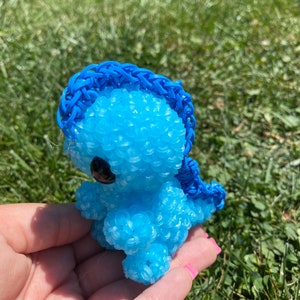 May include: A blue rubber band dinosaur toy with a blue rubber band mane. The dinosaur is made of small rubber bands and has a black eye.