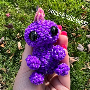 May include: Purple rubber band animal toy with googly eyes. The toy is shaped like a small creature with a horn on its head.