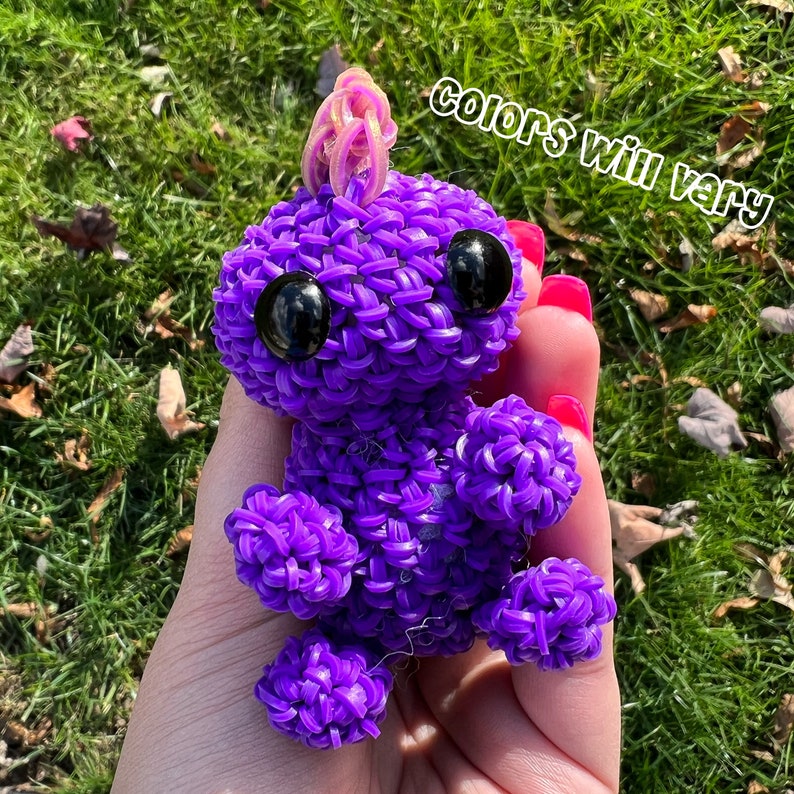 May include: Purple rubber band animal toy with googly eyes. The toy is shaped like a small creature with a horn on its head.