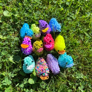 May include: A collection of colorful rubber band ducks, each with a different color and design. The ducks are arranged in a circle on a bed of green grass.
