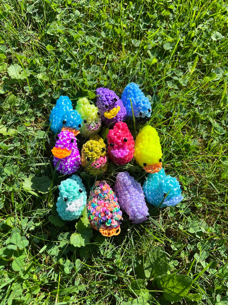 May include: A collection of colorful rubber band ducks, each with a different color and design. The ducks are arranged in a circle on a bed of green grass.