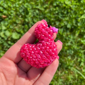 May include: A pink rubber band duck with a purple beak and black eyes. The duck is made of many small rubber bands woven together.